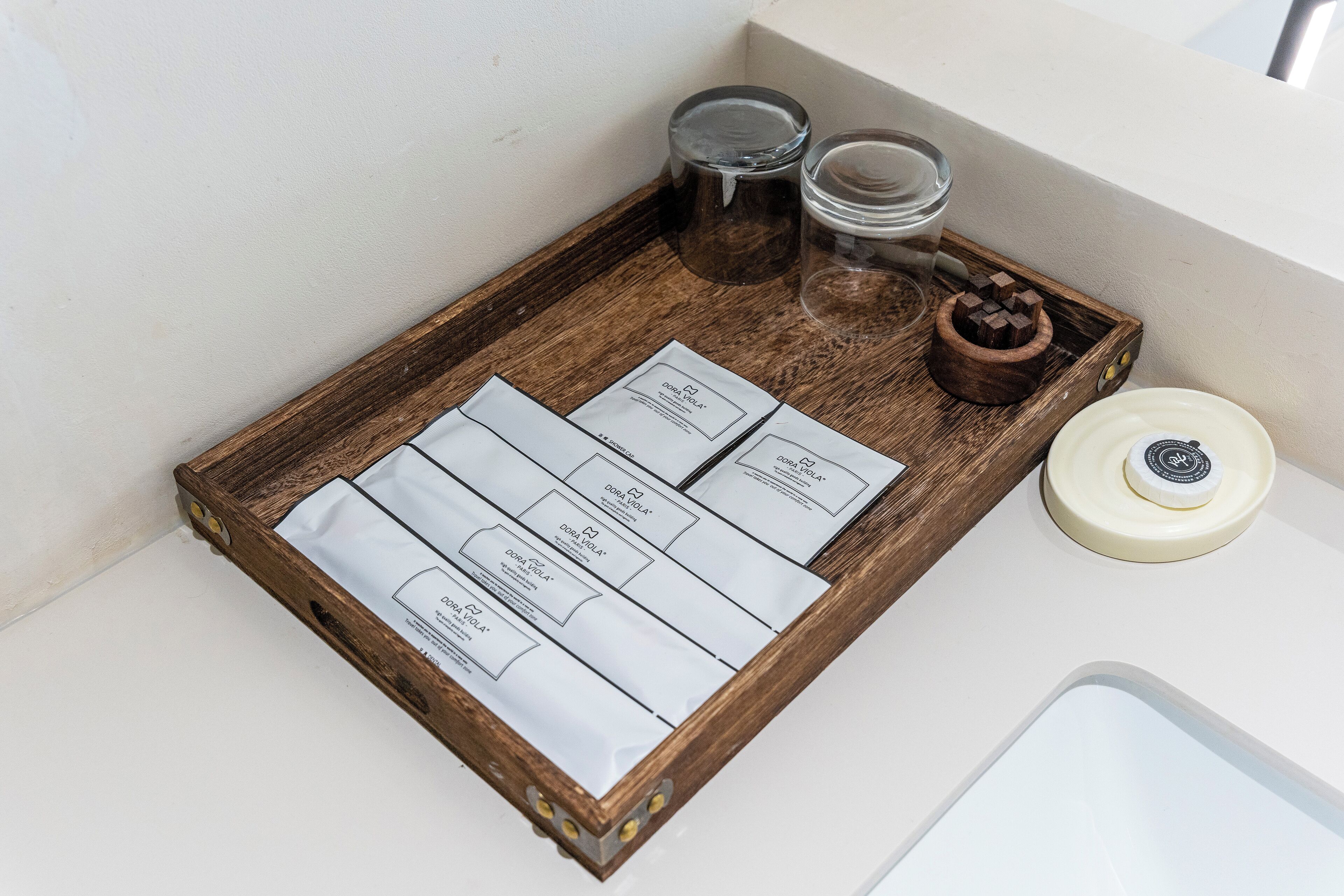 Un plateau contenant quatre cartes blanches, un bol en bois avec un couvercle et deux bouteilles en verre, le tout posé sur une surface en bois.