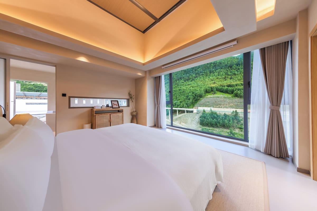 Ein modernes Hotelzimmer mit einem großen Bett, einem Schreibtisch und Blick auf eine üppige grüne Landschaft.