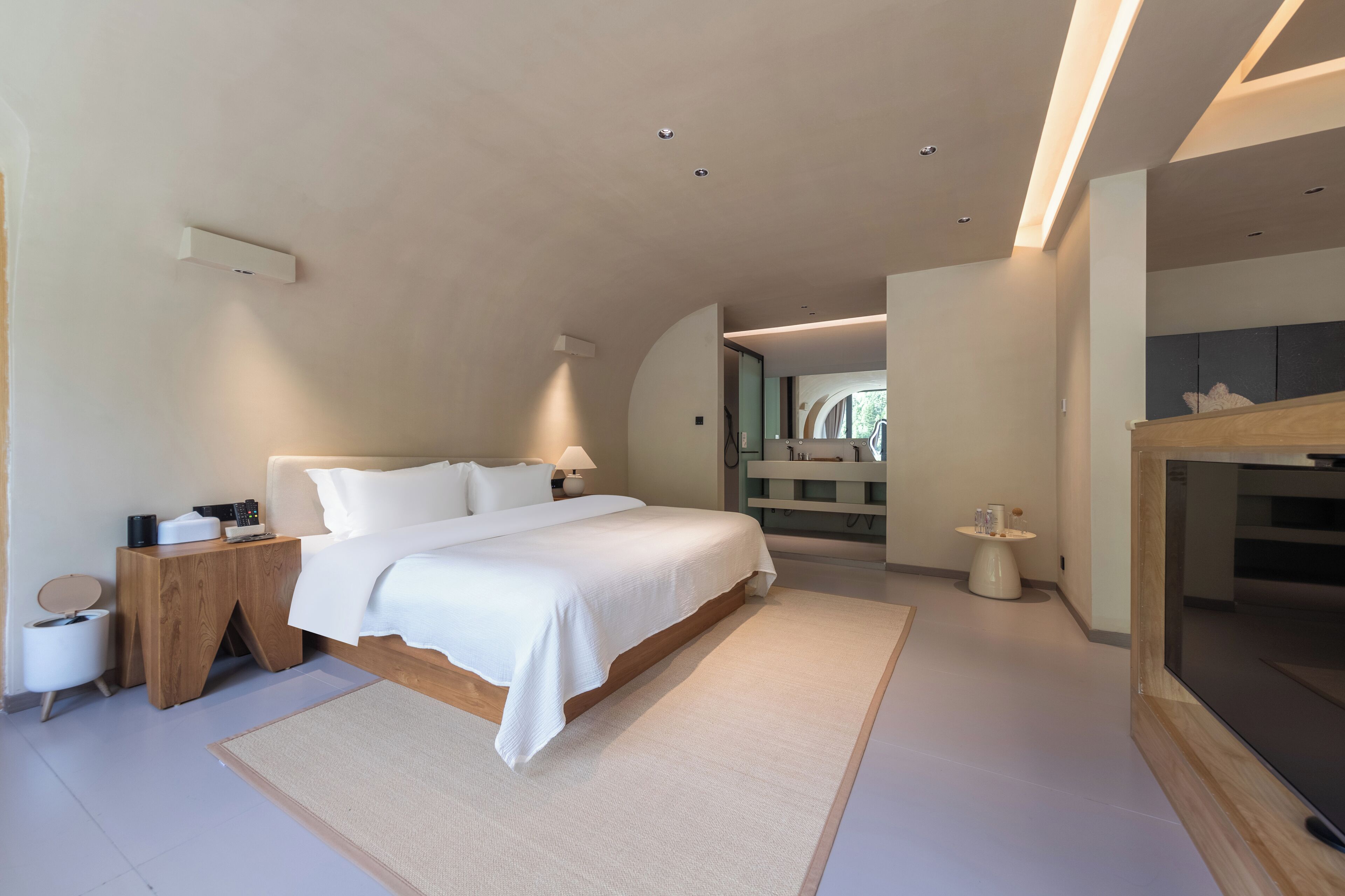 A modern bedroom with a large bed, bedside tables, a TV, and a small side table.