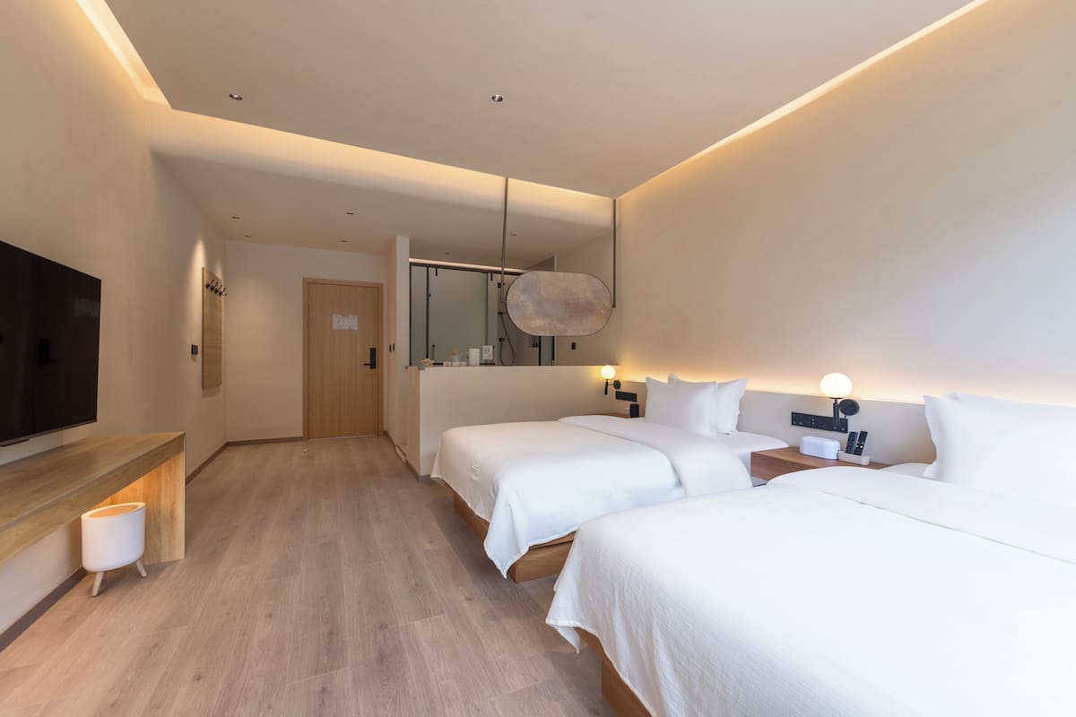 A modern hotel room with two beds, a flat-screen TV, a wooden desk, and a mirror.