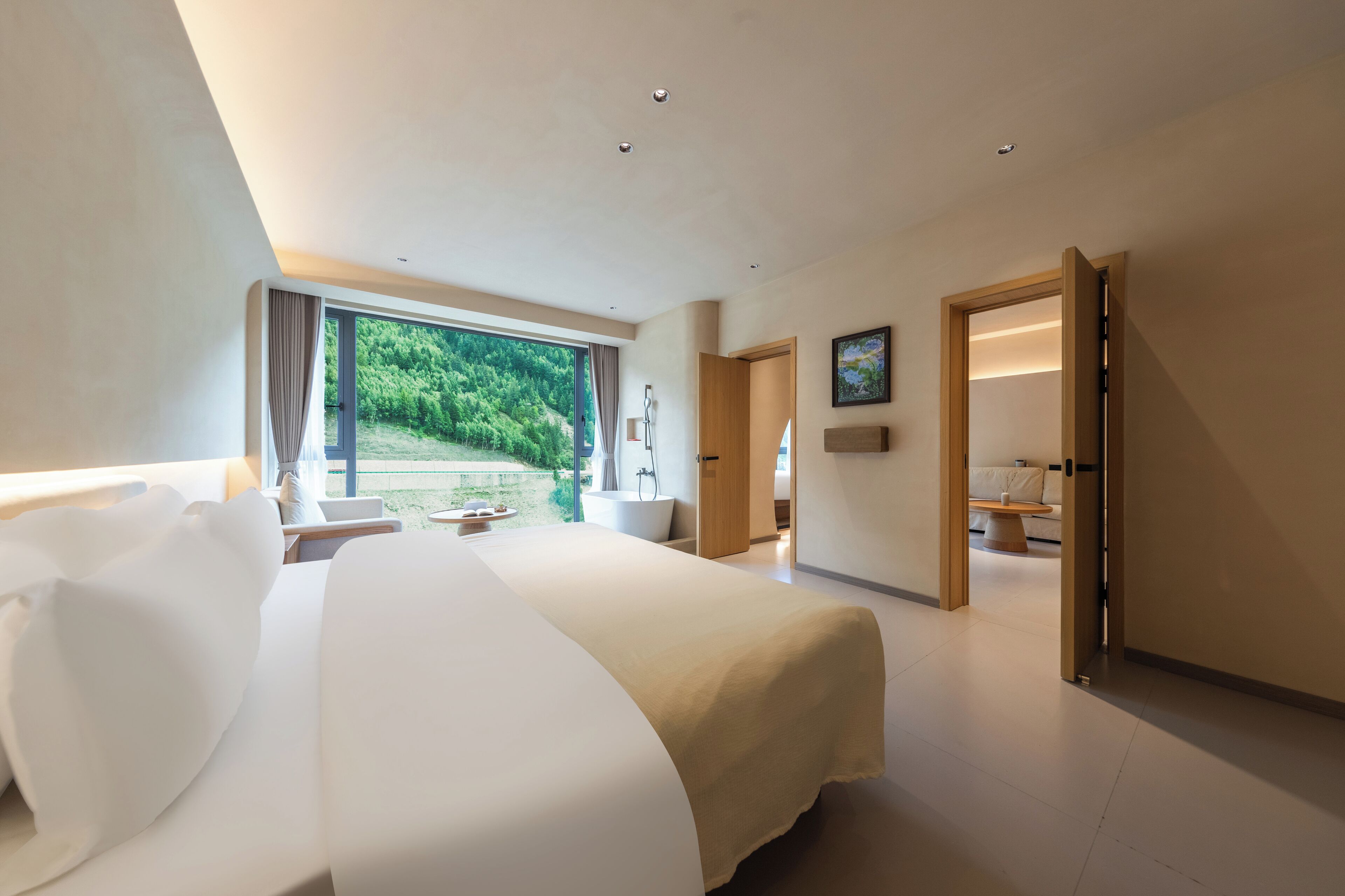 Una moderna camera d'albergo con un letto grande, vista su aree verdi, bagno con vasca e zona salotto con tavolo e sedie.