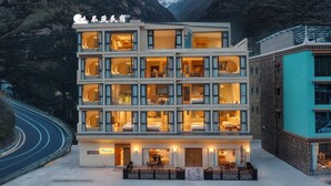 A multi-story hotel with balconies, a well-lit entrance, and a view of a mountainous landscape.