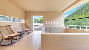 A modern interior with two rocking chairs, a bathtub, and a balcony with a mountain view.