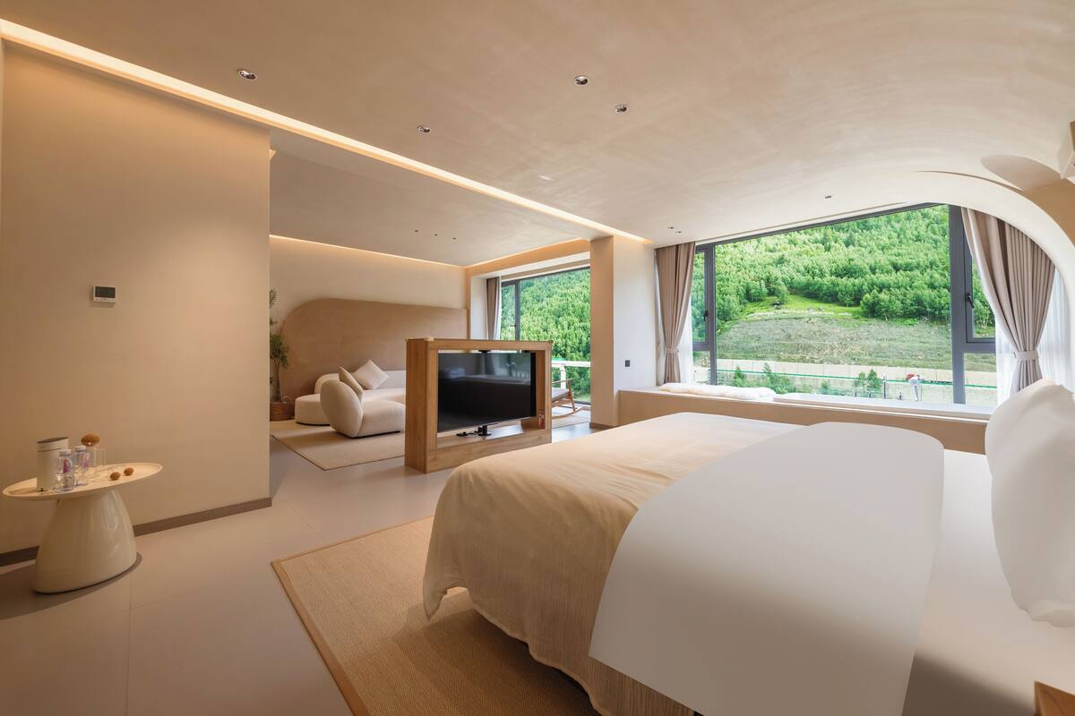 Ein modernes Schlafzimmer mit einem großen Bett, einem Fernseher und Blick auf einen Wald.