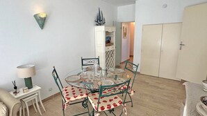 Ein Essbereich mit einem runden Glastisch, vier Stühlen mit floralem Bezug, einem weißen Schrank mit Zierelementen und einer Wandleuchte.