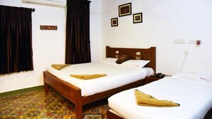 A hotel room with two beds, a ceiling fan, an air conditioner, and a patterned floor. - Rams Inn (Thanjavur)