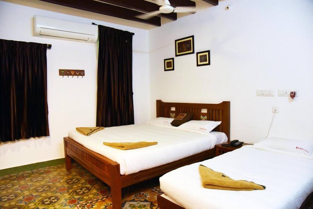 A hotel room with two beds, a ceiling fan, an air conditioner, and a patterned floor.