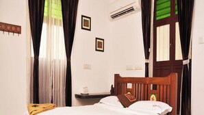 A wooden bed with white bedding, a bedside table, and a wall-mounted air conditioner. - Rams Inn (Thanjavur)