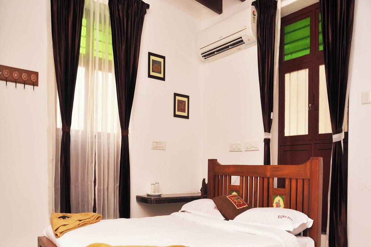 A wooden bed with white bedding, a bedside table, and a wall-mounted air conditioner.