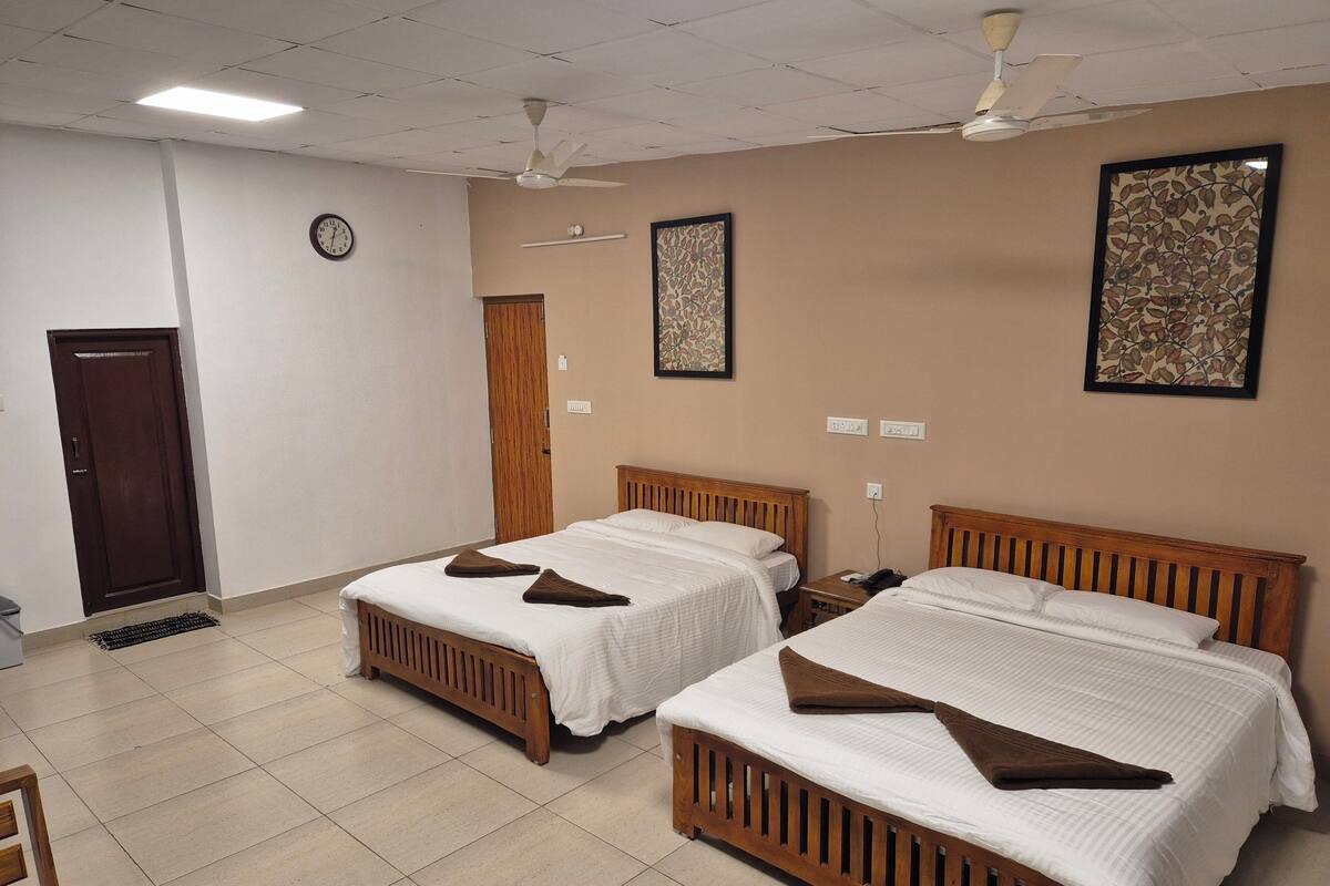 A hotel room with two wooden beds, a ceiling fan, a clock, and a door.