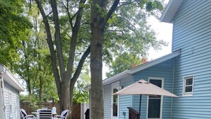 A backyard with a wooden deck, outdoor furniture, and a tree. - 15 mins to Notre Dame; visit The Cozy Blue Haven in Niles, MI (Niles)