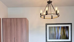 Een kamer met een houten garderobe, een bureau met stoel, een ingelijste foto aan de muur en een moderne kroonluchter.