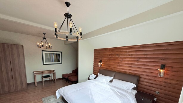 Een moderne slaapkamer met een groot bed, een houten hoofdbord, een bureau, een stoel en een kroonluchter.