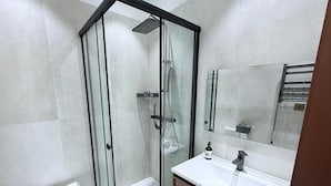 Une salle de bain moderne avec une douche à parois de verre, un lavabo blanc et un grand miroir.