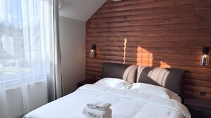 Une chambre d’hôtel moderne avec une tête de lit en bois, un lit bien fait avec du linge de lit blanc et une fenêtre ornée de rideaux légers.