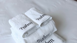 Une pile de serviettes soigneusement pliées, portant le nom « Fahrn » brodé dessus, est posée sur un lit recouvert de draps blancs.