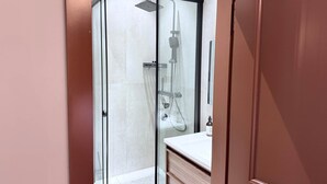 A glass-enclosed shower with a handheld showerhead, a wall-mounted faucet, and a handheld showerhead.