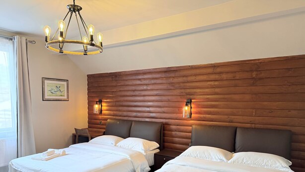 A hotel room with two beds, a wooden headboard, a chandelier, and a framed picture on the wall.