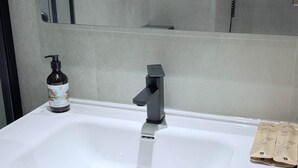 A bathroom sink with a modern faucet, a bottle of liquid soap, and two small brown paper bags.