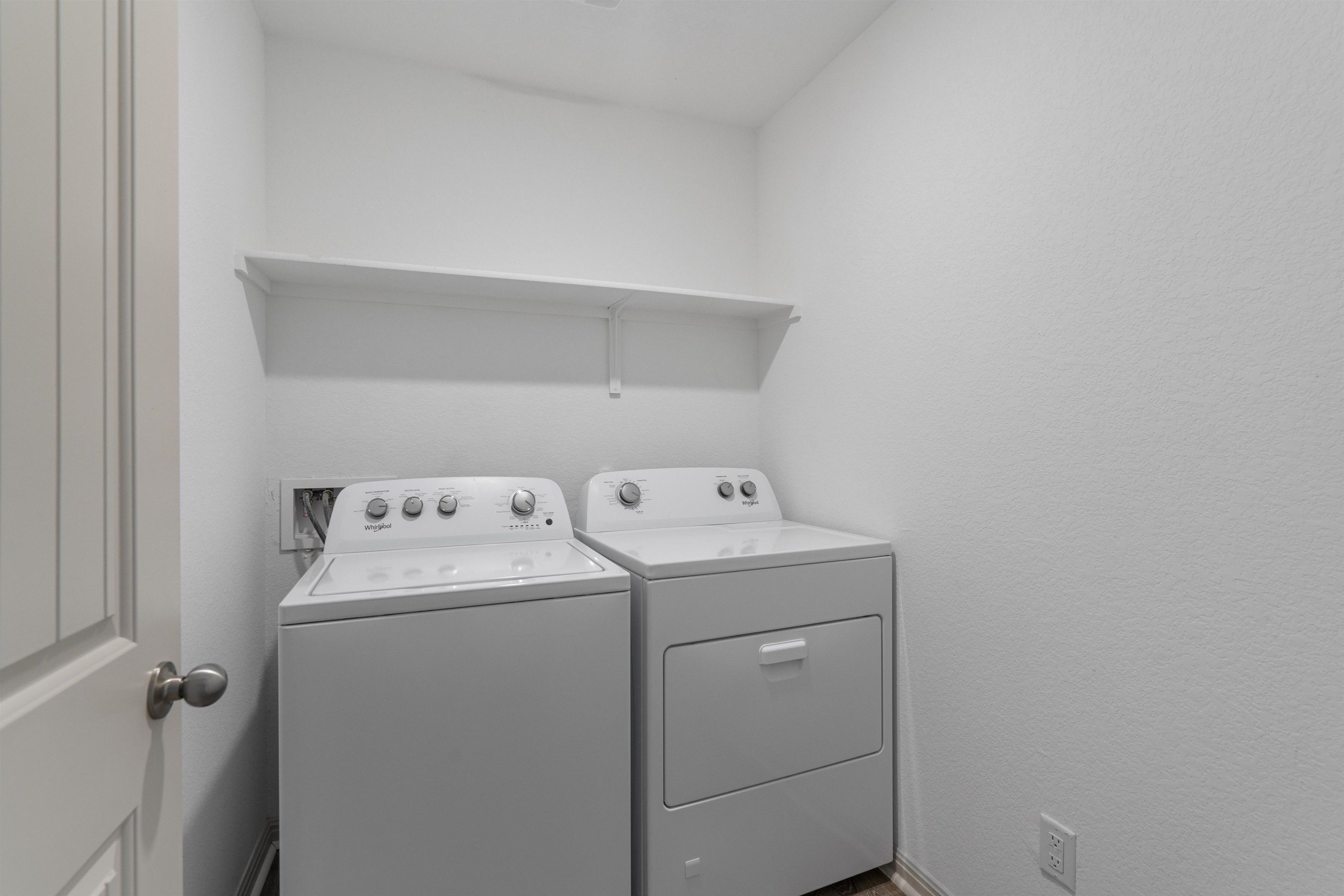 A laundry room with two stacked washers and dryers, a white door, and a small shelf above the dryers.