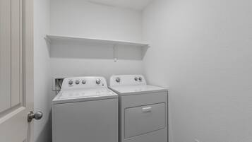 A laundry room with two stacked washers and dryers, a white door, and a small shelf above the dryers.