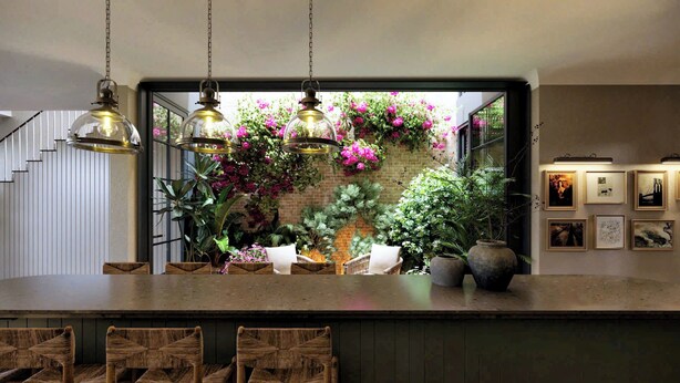 A bar area with a rustic wooden counter, hanging pendant lights, and a brick wall adorned with flowering plants.