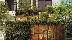 A modern two-story building with a brick facade, large windows, and a metal fence with a view of a garden.