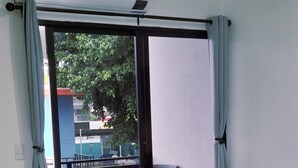 Une pièce dotée d’une porte-fenêtre coulissante qui donne sur un balcon. On y trouve une chaise et une petite table, ainsi qu’une plante sur le balcon.