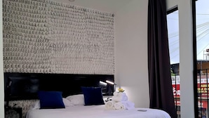 Une chambre d’hôtel moderne avec un grand lit, une tête de lit au motif texturé, une table de chevet noire, une table de chevet blanche et un tapis à motifs noir et blanc.