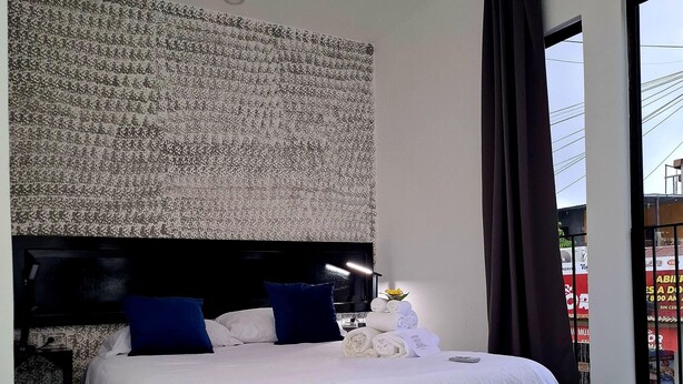 Une chambre d’hôtel moderne avec un grand lit, une tête de lit au motif texturé, une table de chevet noire, une table de chevet blanche et un tapis à motifs noir et blanc.