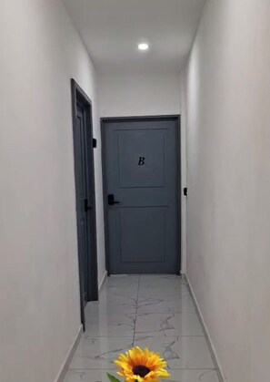A hallway with a closed door marked with a 'B' and a sunflower graphic with text welcoming to The Bello Lodging. - Bello Lodging Downtown Juayúa (Juayua)