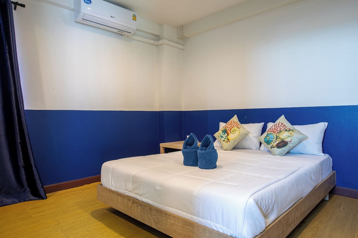 Une chambre d’hôtel avec un lit, une table de chevet, une décoration aux couleurs bleu et blanc, et un climatiseur fixé au mur.