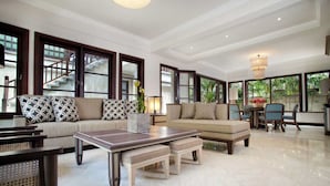 A spacious living area with a sofa, coffee table, and chairs. Large windows provide natural light and views. - Sundara Oceanside Villa (Tabanan)