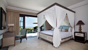 A spacious bedroom with a four-poster bed, a desk, and a chair, featuring a large window and a view of the ocean. - Sundara Oceanside Villa (Tabanan)
