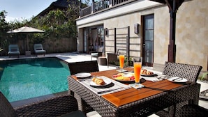 A poolside dining area with wicker furniture, a table set with plates, croissants, and orange juice glasses. - Sundara Oceanside Villa (Tabanan)