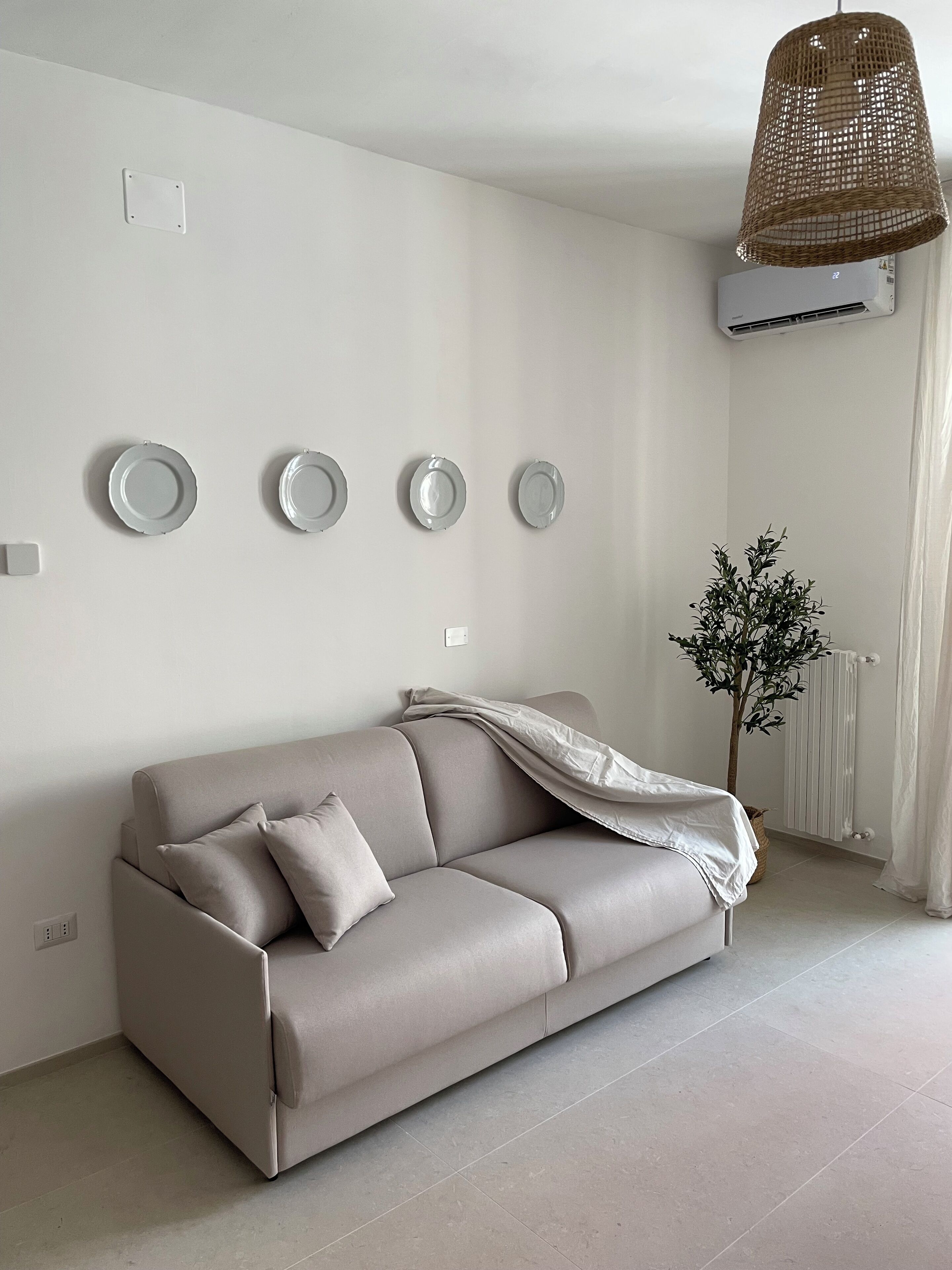 Una sala moderna con un sofá color beige, una lámpara colgante tejida y un radiador.