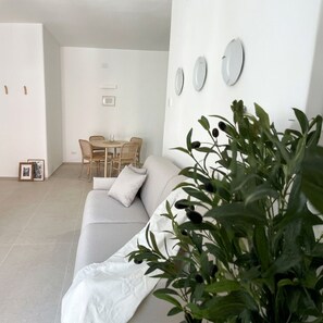 A modern living room with a sofa, a dining table with chairs, and a potted plant.