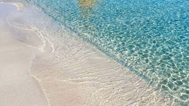 Uma praia calma com uma rocha grande em alto-mar.