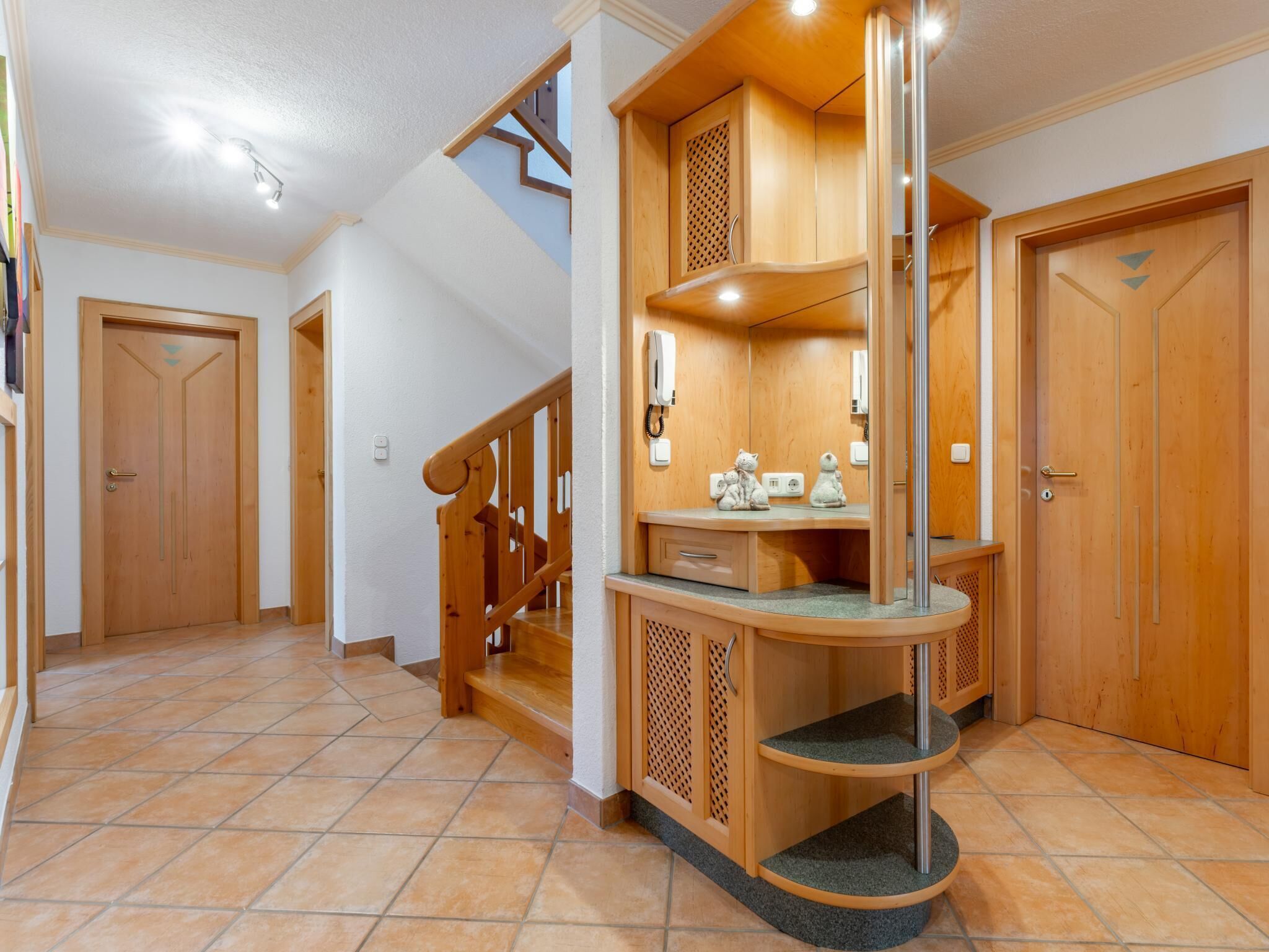 Un hall d’entrée spacieux avec un escalier en bois, un bureau intégré avec un téléphone et une porte ornée d’un motif décoratif.