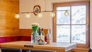 A dining area with a wooden table, four chairs, a vase with flowers, and bottles of wine. - Detached holiday home with terrace and balcony. (Bramberg am Wildkogel)