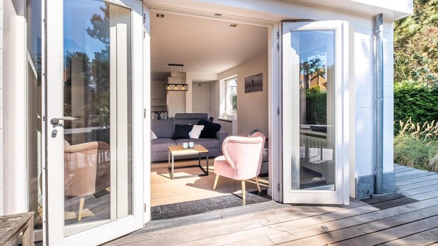 Een moderne, open woonkamer met een bank, een roze fauteuil en een klein tafeltje.