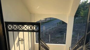 Eine Treppe führt zu einem Balkon mit einem Metallgitter, Blick auf eine Straße mit einem Geschwindigkeitsbegrenzungsschild und einem wolkenlosen Himmel.