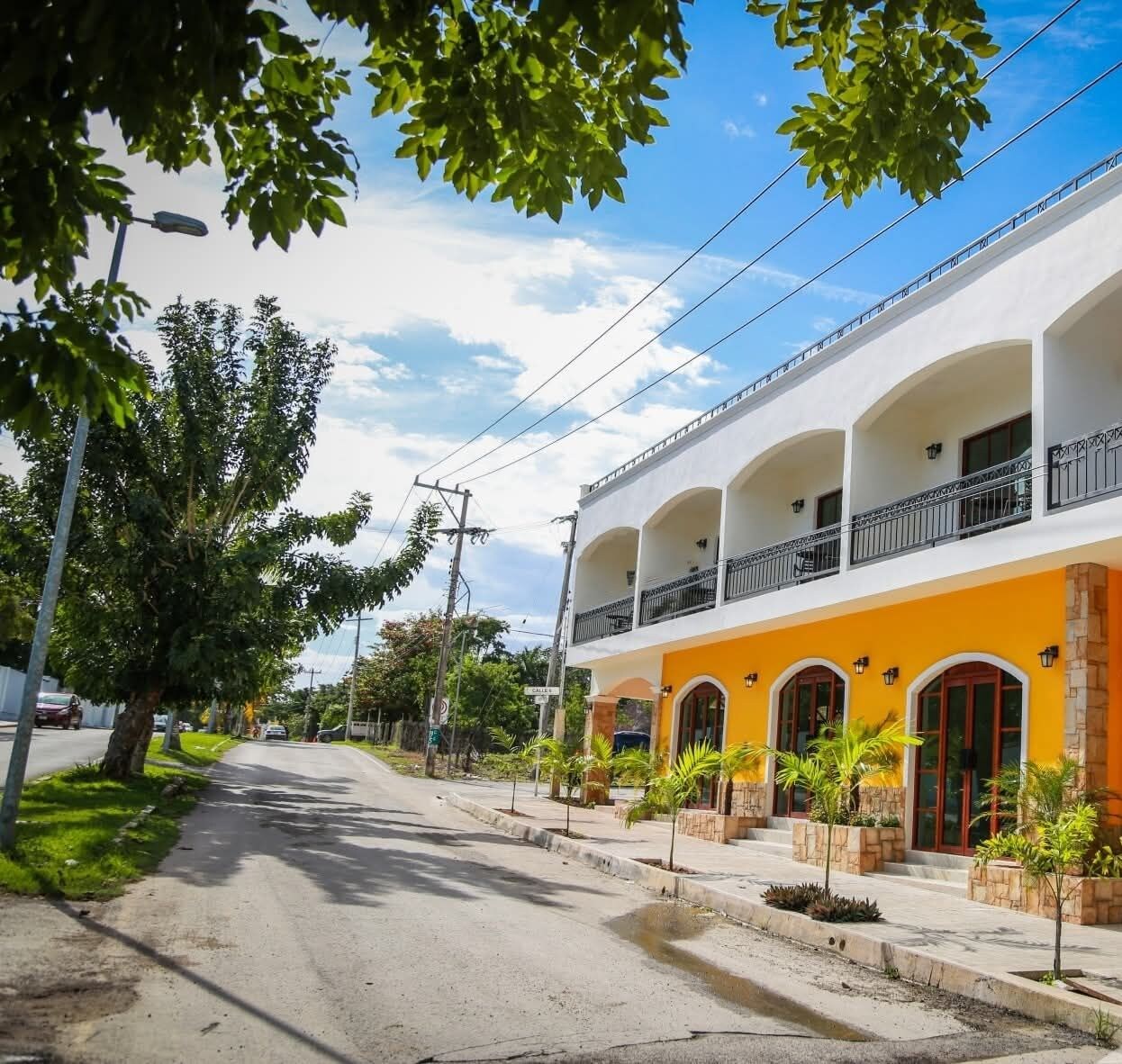 Ein zweistöckiges Hotel mit weiß-orangener Fassade, mehreren Balkonen und einer gepflasterten Straße mit Bäumen.