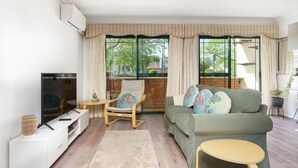 Un salon avec un canapé, un fauteuil, une petite table et un téléviseur.