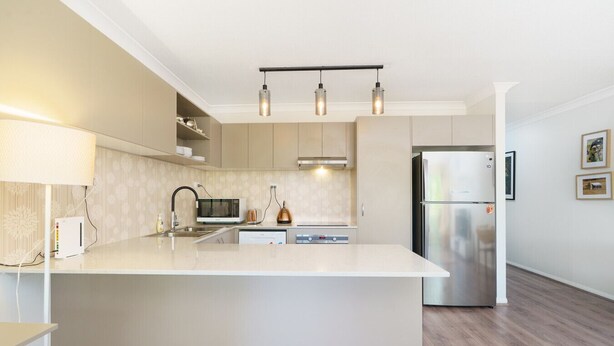 Une cuisine moderne dotée d’un îlot central, d’appareils électroménagers en acier inoxydable et de luminaires suspendus.