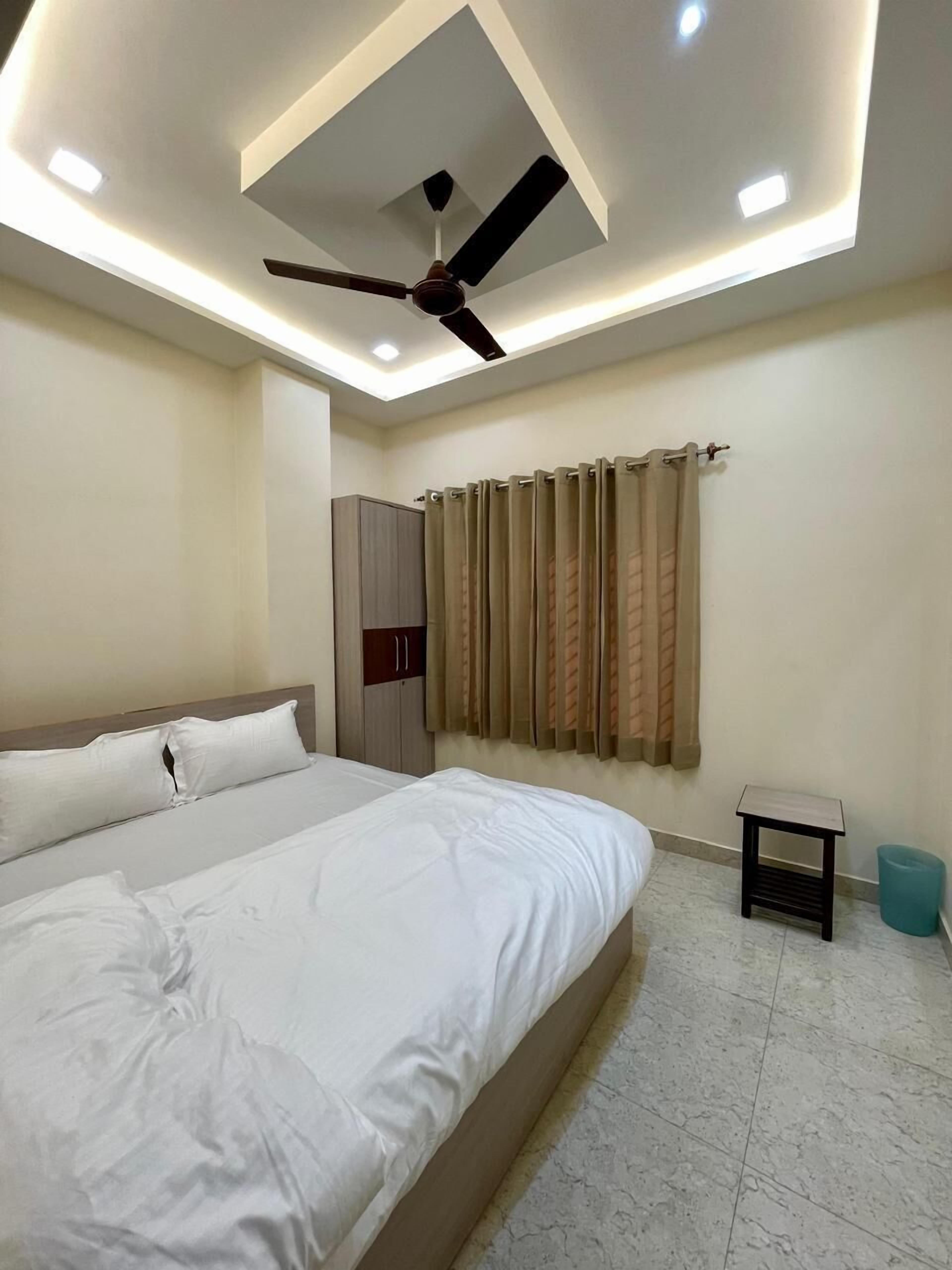A bedroom with a bed, a ceiling fan, a wardrobe, and a window with curtains.