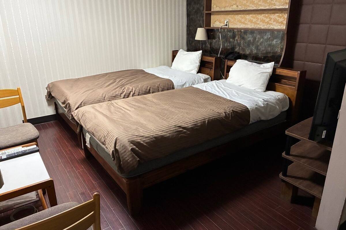 Een hotelkamer met twee enkele bedden, een bureau met stoel, een televisie en een wandplank.