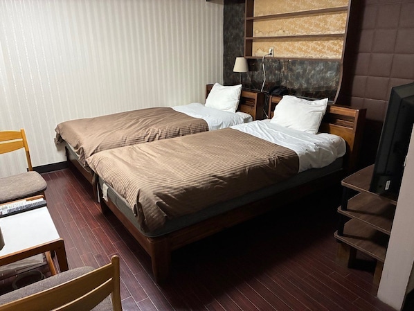 A hotel room with two single beds, a desk with a chair, a television, and a shelf unit. - MITO DAIICHI HOTEL BEKKAN (Mito)