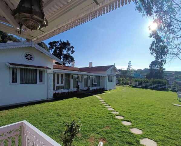 A white building with a covered porch and a well-maintained lawn with stepping stones. - Brooklyn Villa (Ooty)