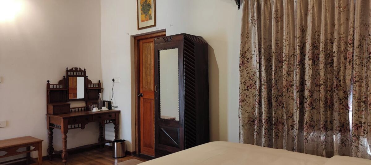 A room with a bed, a wooden desk with a mirror, a door, and a curtain.